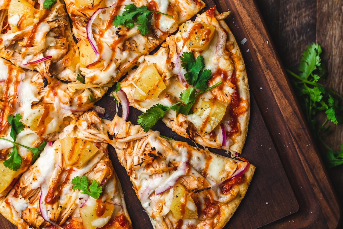 A wood-fired pizza emerging from a stone oven with flames behind it.